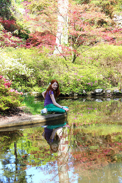 ragazza seduta in stagno guardando testa di koi pesce nuotare - formal garden ornamental garden child single flower foto e immagini stock