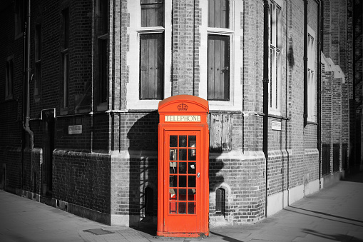 A traditional red telephone booth in the streets of London, centered betweem two windows