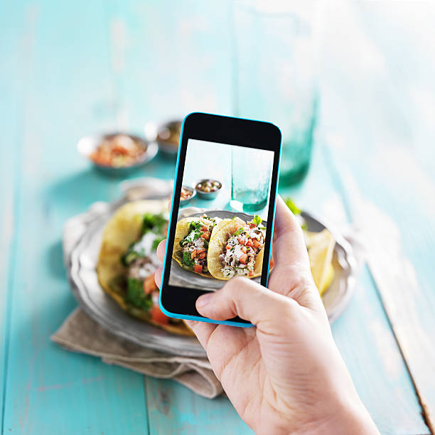 taking photo of carnitas street tacos with smart phone taking photo of carnitas street tacos with smart phone with focus on phone. plate photos stock pictures, royalty-free photos & images