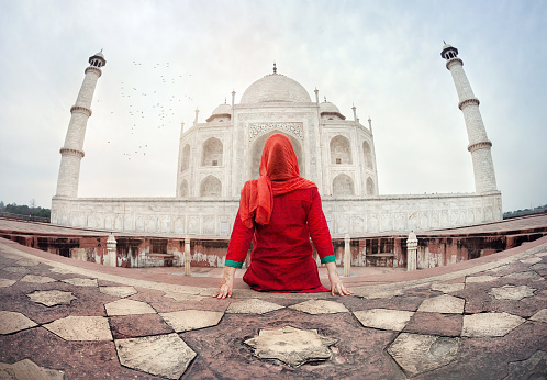 Woman in red costume sitting on the floor and looking at Taj Mahal in Agra, Uttar Pradesh, India