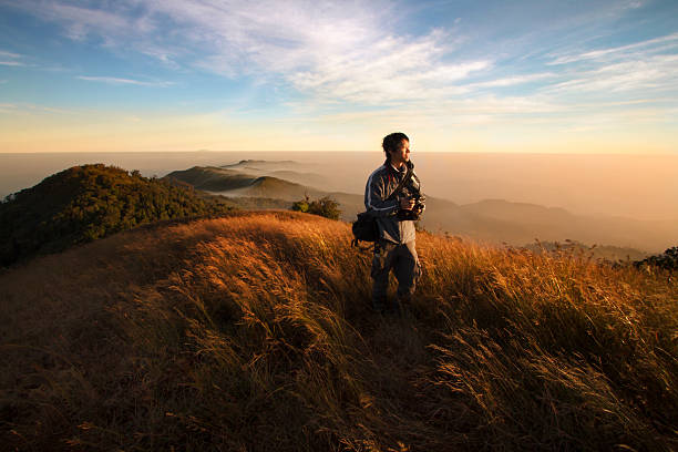 Traveler on beautiful mountain and sunrise. Traveler holding the camera walking in the meadow on top of mountain that around with beautiful view of morning sunrise and blue sky. nature and landscapes camera stock pictures, royalty-free photos & images