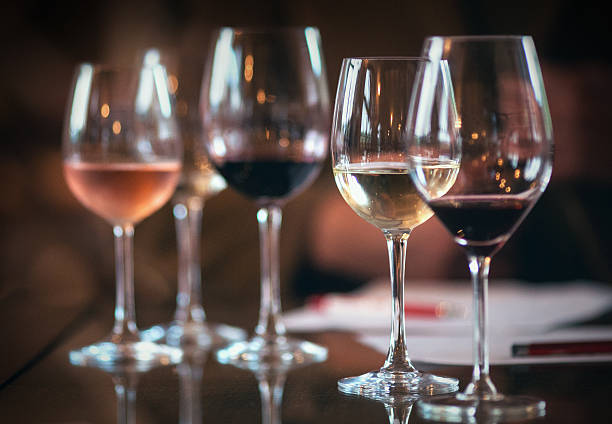 WIneglasses with different kinds of wines. Closeup of five wineglasses arranged one next to the other, half full with several sorts of wines, red, white and rose wines. Glasses are on the table, there are some papers and pens in background as this was the detail from winetasting. Lit from both sides. winetasting rose wine wineglass elegance stock pictures, royalty-free photos & images