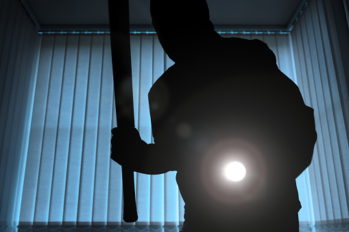 Burglar or intruder inside of a house or office with flashlight and baseball bat