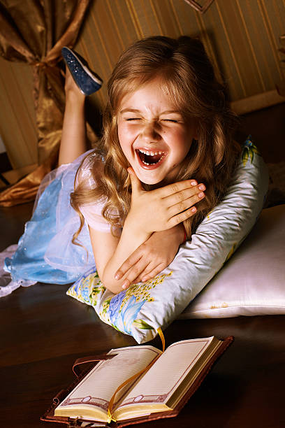 Little smiling girl in a blue dress lies on the floor in room, beside her is a book