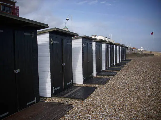 Bexhill on sea shingle beach with beach huts. Blue sky with clouds as background.