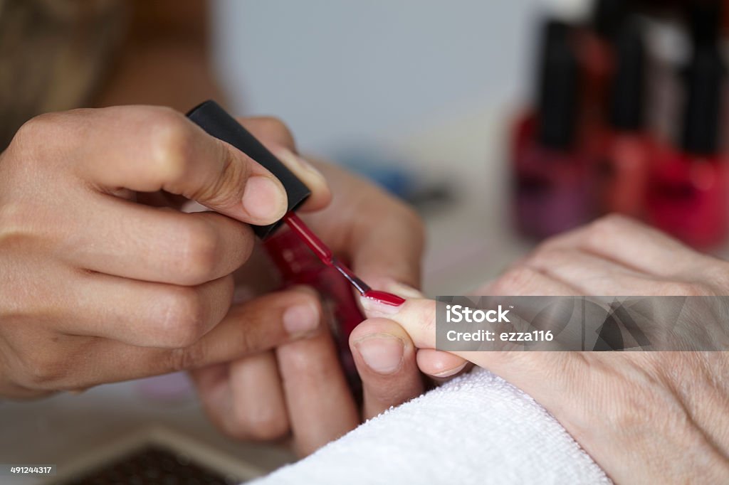 Woman In Beauty Salon Having Nails Treated Woman in nail salon having her nails painted by a mixed race beautician - close up detail Adult Stock Photo