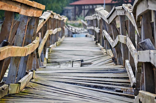 Closeup of a deformed and dilapidated wooden bridge over the small river. Weathered and broken wood planks of a very old and damaged pedestrian bridge near the village.