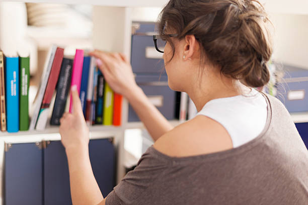 istock Woman choosing favourite book from home library 491246455