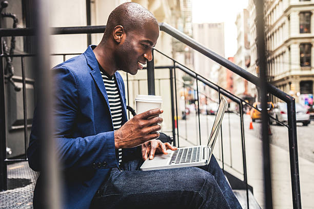 hombre enviando mensajes de texto en computadora portátil sentado en pasos en las calles - sidewalk cafe fotografías e imágenes de stock