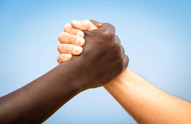 Black and white human hands - Handshake against racism Black and white human hands in a modern handshake to show each other friendship and respect - Arm wrestling against racism blue brothers stock pictures, royalty-free photos & images