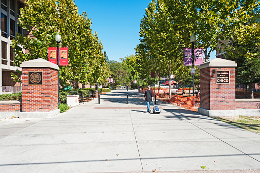 Chico, California, USA - October 4, 2015: This woman and the other men and women are walking along the entranced to the Chico California State University, the campus is situated in community of Chico in Northern California a smaller but very vibrant community in the North State area and on this very comfortable autumn day  it was relaxing to just drive around and enjoy the various sites of this campus and the community with many mature neighborhoods.
