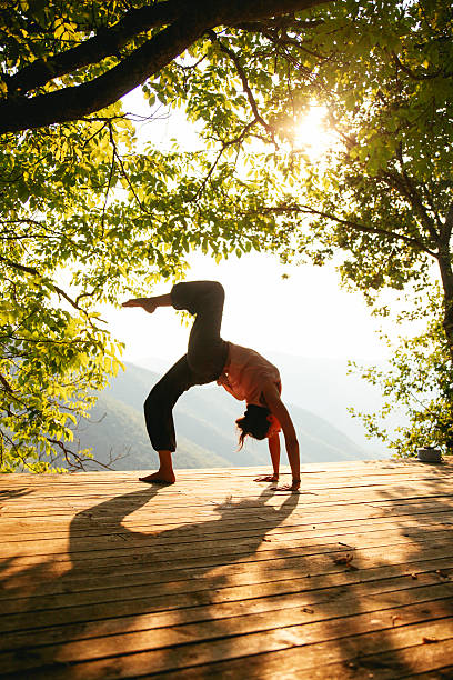 Young woman practicing yoga or doing just a stretching exercise next to the beautiful view on the canyon. She is wearing oriental trousers and a nude shirt. Taken by the Bosnian Croatian border, in the Dinara mountains, South Eastern Europe. A wooden terrace is made just next to the trees, lit by sun, a perfect place for meditation, exercise, yoga practice or just relaxation.