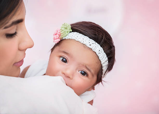 Closeup portrait of cute adorable little baby girl peeking over his shoulder mother, wearing nice head accessory, happy young family concept