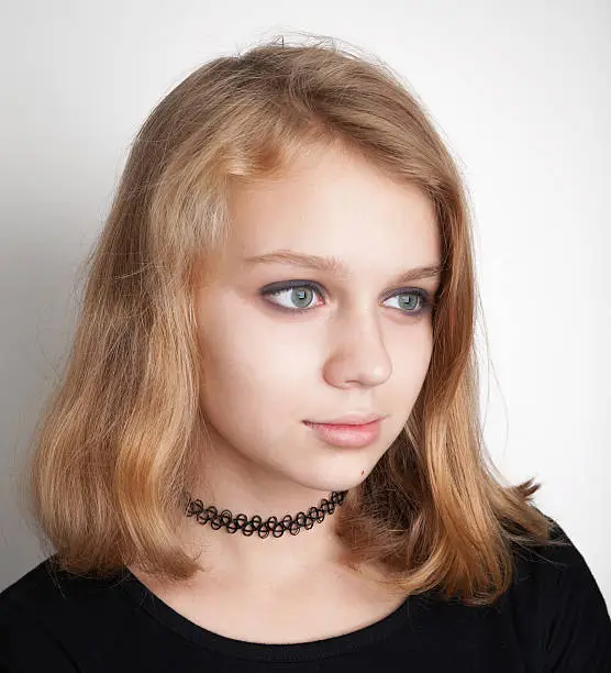 Beautiful Caucasian blond teenage girl in black choker necklace. Studio portrait over white background with soft shadow
