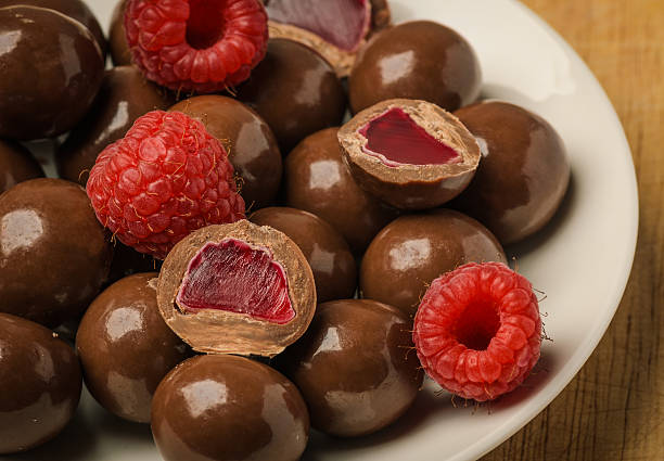 Milk chocolate coated jelly candies and fresh raspberry on white plate