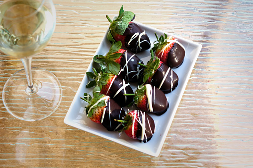 A plate of strawberries in chocolate on a glass surface with a glass of wine