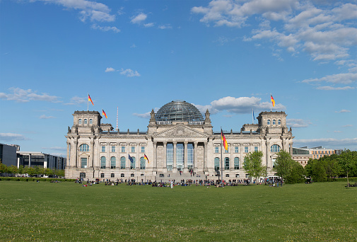 The German Reichstag (house of parliament) in Berlin with flags and Dome. Some people in front of. German parliament.