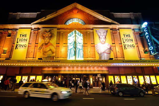 Sydney, Australia - May 15, 2014: A taxi leaves after dropping off a passenger at historic Capitol Theatre on Campbell St at night. Other patrons are gathered around the entrance, awaiting a performance of Disney's The Lion King. 