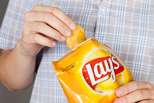 Tambov, Russian Federation - January 20, 2013: Hand takes out potato chip from Lay's bag. It is a potato chips with cheese. Studio shot.
