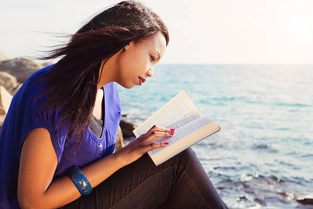 chica joven mirando su biblia en el mar - reading religious text black bible fotografías e imágenes de stock