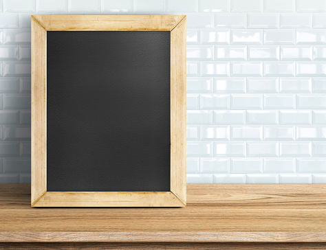 Blank blackboard on tropical wooden table at white tile wall,Template mock up for adding your design and leave space beside frame for adding more text.