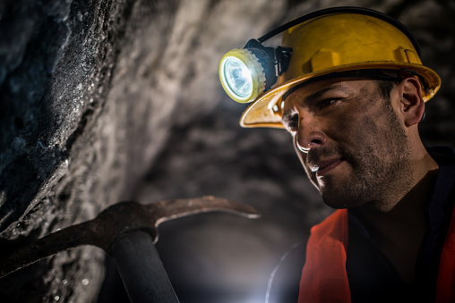 Miner working at a mine underground wearing a helmet with light and using one of his tools