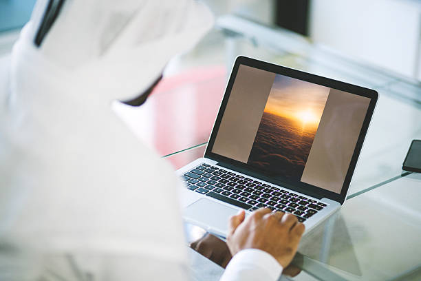 Emirati Man Using Laptop at Home Over the shoulder view of Arab man using his laptop in a modern living room. emirati culture photos stock pictures, royalty-free photos & images