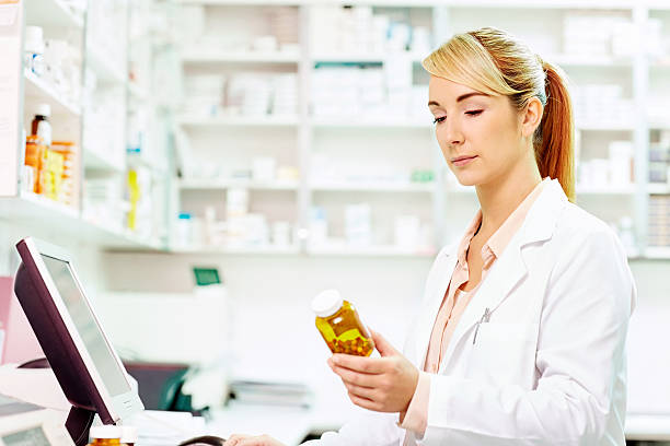 istock Pharmacist reading label on pill bottle at desk 491365316