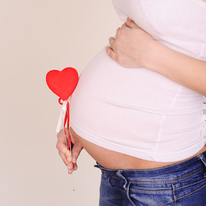 Pregnant woman holding red heart close up on white background