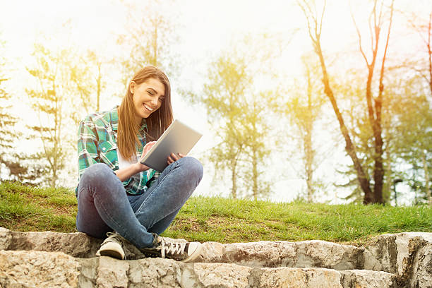 Feliz mujer joven con tableta digital sentado en el parque - foto de stock