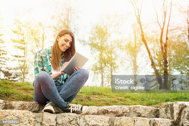 Happy Young Woman With Digital Tablet Sitting In Park Stock Photo - Download Image Now
