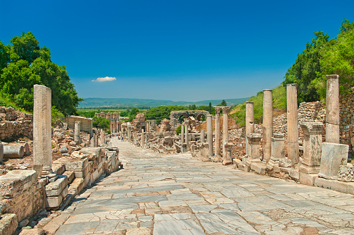 marble alley with columns leading to the Celsus Library in ancient greek city of Ephesus with mountains and clear blue sky at background with single small cloud over the Celsus Library, Turkey