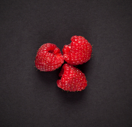 Three raspberries on black background. Top view.
