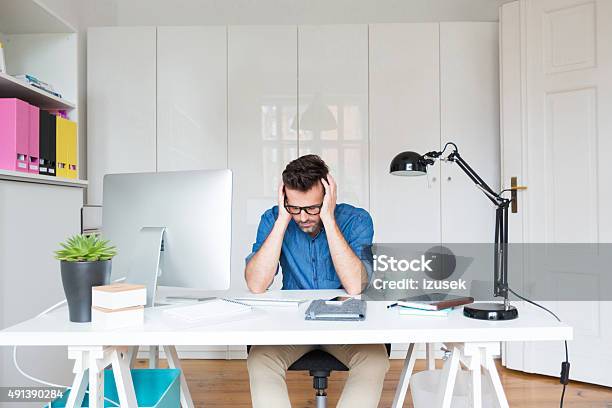 Sad Man Sitting At The Desk With Head In Hands Stock Photo - Download Image Now - Office, 2015, Adult