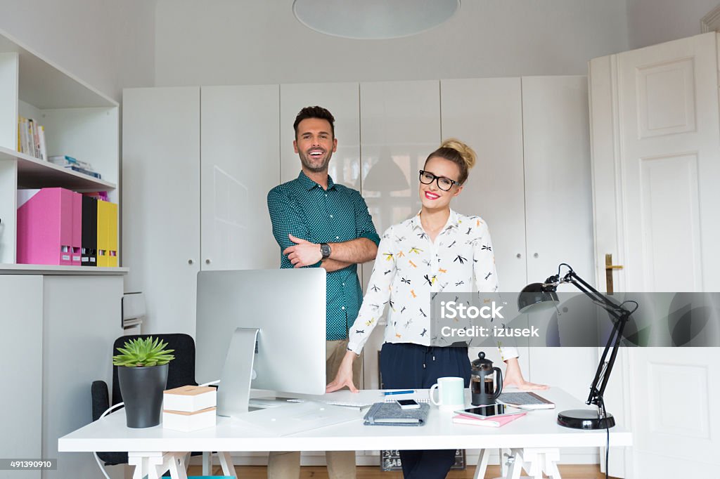 Woman and man in an office Woman and man standing behind the desk in a small office and smiling at the camera.  2015 Stock Photo