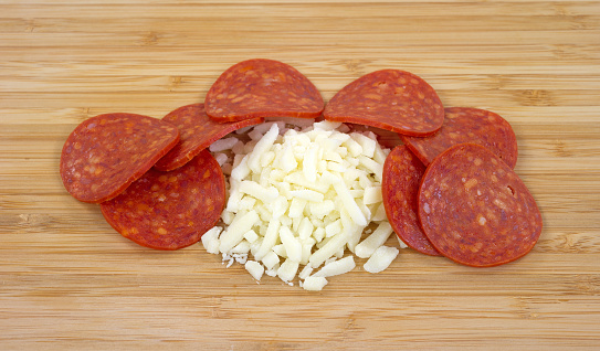 A small portion of mozzarella cheese surrounded by slices of pepperoni on a wood cutting board.
