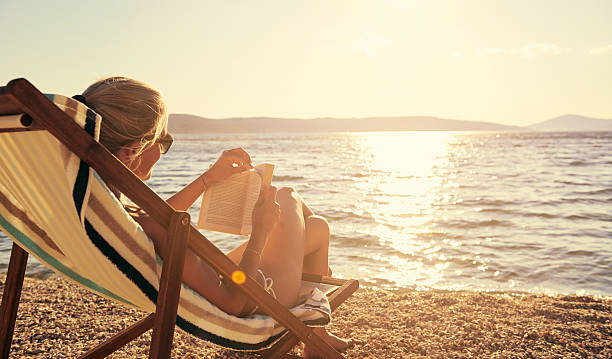 Relaxing with a good book in beautiful surroundings A young woman reading a book while sitting on a chair at the beachhttp://195.154.178.81/DATA/i_collage/pu/shoots/805670.jpg sunbathing stock pictures, royalty-free photos & images