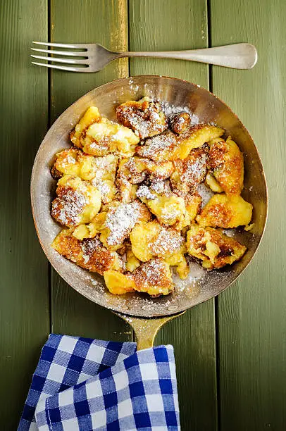Kaiserschmarrn with icing sugar in a metal pan standing on a green wooden table