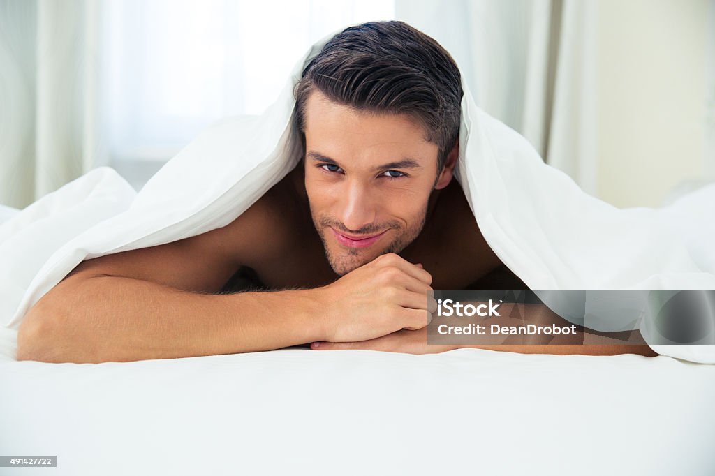 Man lying under blanket in the bed Portrait of a happy man lying under blanket in the bed at home 2015 Stock Photo