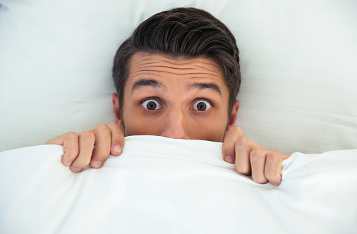 Man hiding in bed under the blanket at home