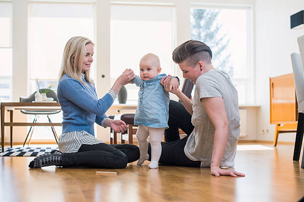 Lesbian couple assisting baby to walk at home A photo of lesbian couple assisting baby to walk. Homosexual couple is with cute toddler at home. Family of three is at brightly lit room. unknown gender stock pictures, royalty-free photos & images