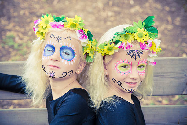 Cute twin girls with sugar skull makeup Cute twin girls smiling with sugar skull makeup on a wooden bench halloween face paint stock pictures, royalty-free photos & images