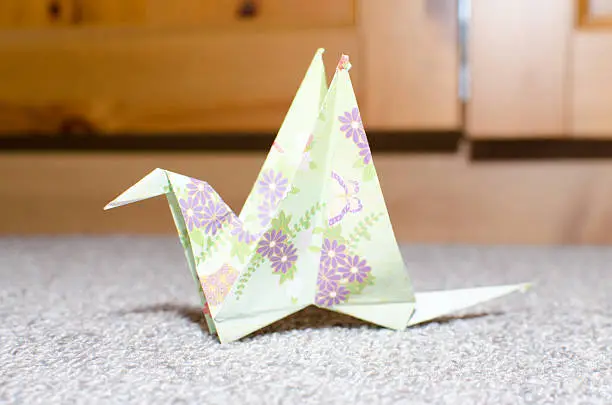One paper folding, origami of a bird closeup on a grey carpet