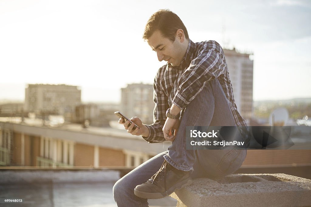 Urban young man using a smart phone Young man listen to the music on smartphone on the top of building with city in beckground Adult Stock Photo