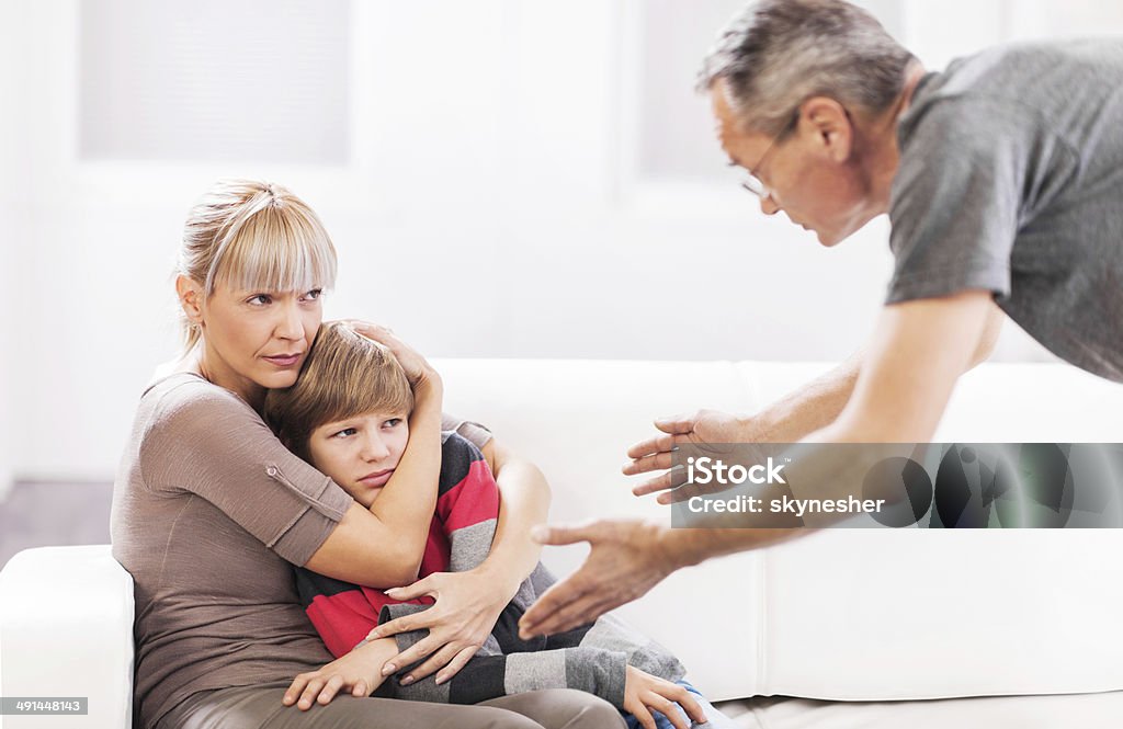 Mother defending her son while father is scolding him. Mature father is scolding his son while mother is defending him.    Adolescence Stock Photo