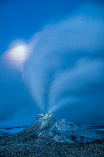 A fumarole vent erupts with hot steam at night under a full moon at Hveravellir, a remote mountainous geothermal area in the Interior of Iceland that is only accessible in the summer months, Kjolur Route, Iceland