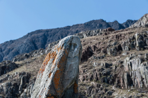 Ancient reindeer stone with a face of a warrior on a background of mountains and sky