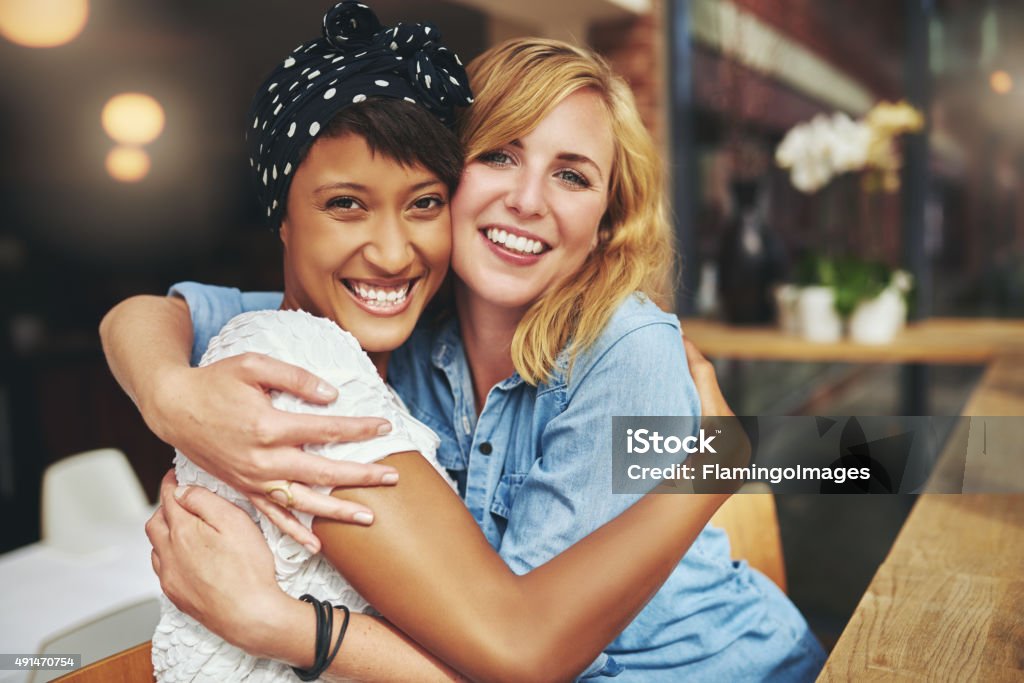 Two happy affectionate young woman hugging Two happy affectionate young woman hugging each other in a close embrace while laughing and smiling, young multiracial female friends Gay Couple Stock Photo