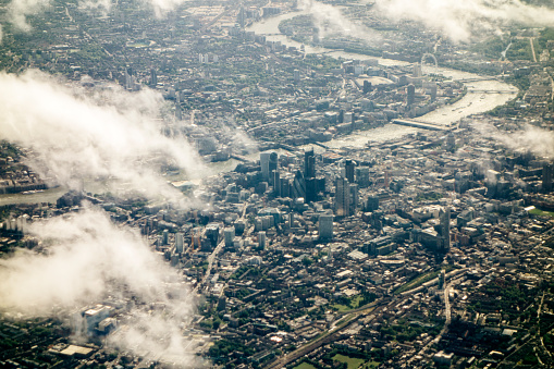 An aerial view of London, the City of London, River Thames and Thames Bridges and the London Eye, visible in the far distance, taken from within an aeroplane. Daylight, nobody, horizontal composition. Clouds. 