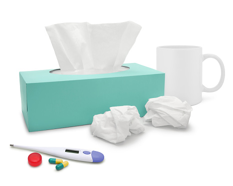 Cold and flu themed image. Tissue box, thermometer, cough lozenge, capsules and a hot drink isolated on white.